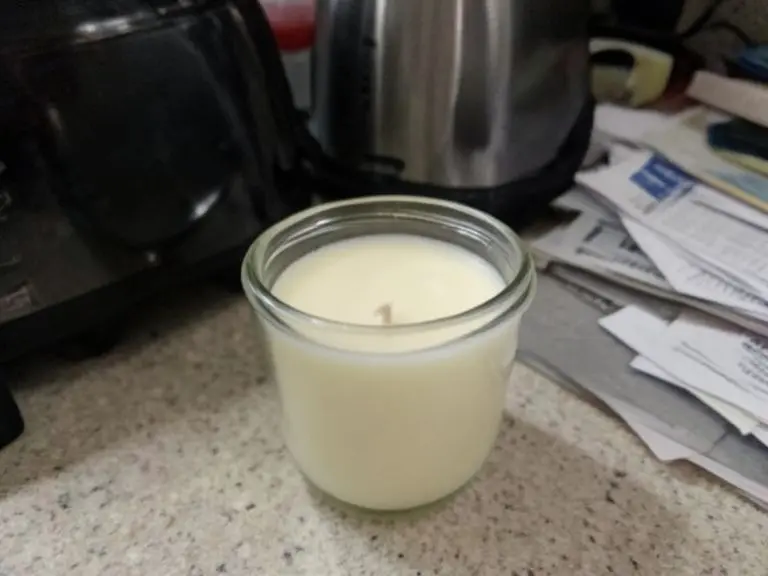 Unlit cream candle in a clear glass jar on a kitchen counter next to a toaster and mail