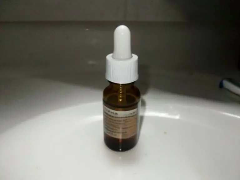 Amber glass dropper bottle with a white cap on a white bathroom sink under harsh light